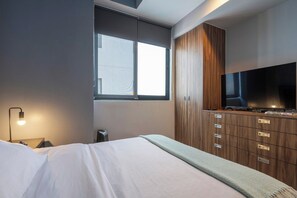 Ein modernes Schlafzimmer mit Bett, Fernseher, Kleiderschrank und Fenster.