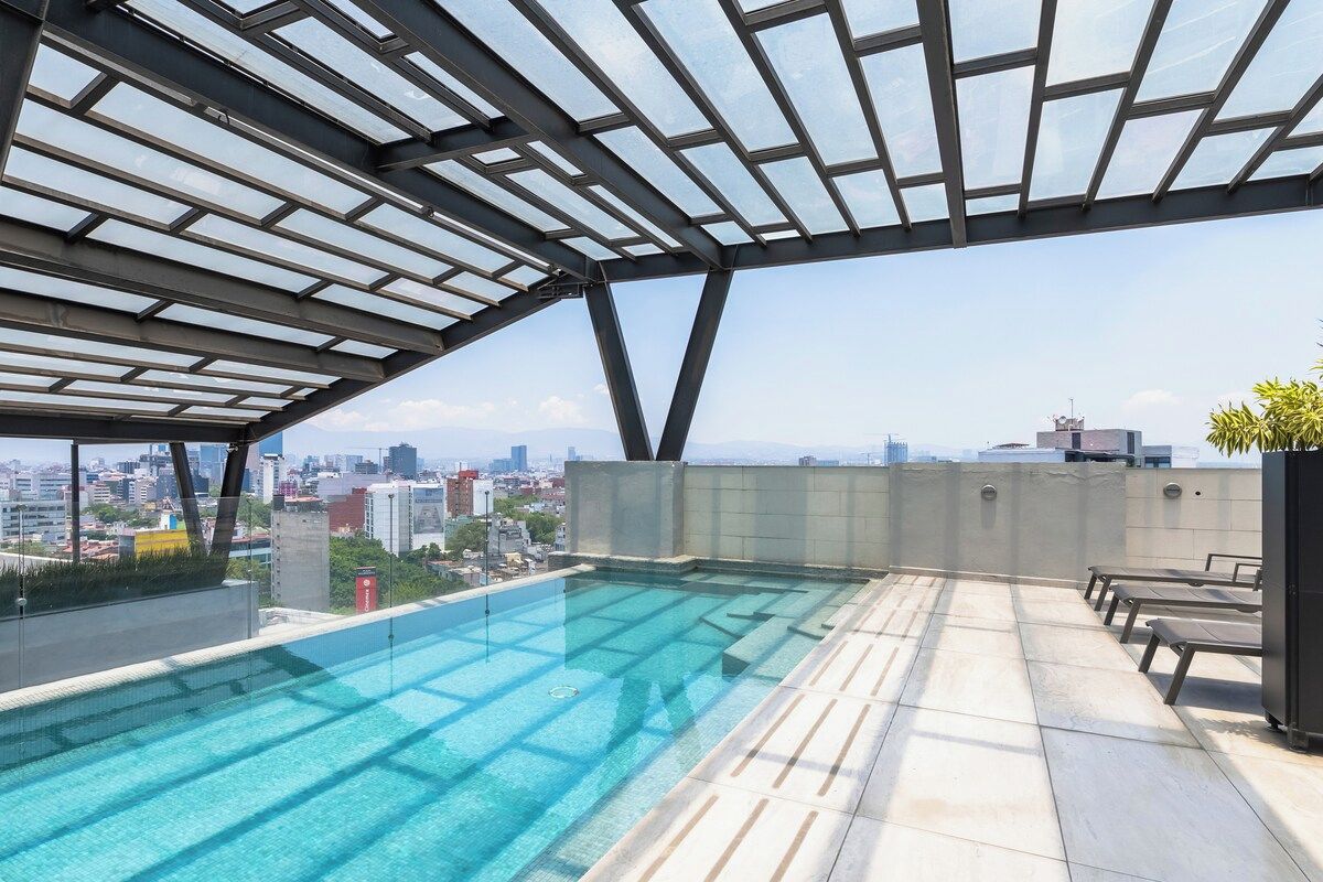 A rooftop infinity pool with a glass ceiling, offering a city view.