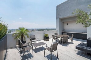 Eine Dachterrasse mit Sitzgelegenheiten im Freien, einer kleinen Palme und Blick auf die Stadtlandschaft.