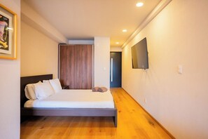 Ein Schlafzimmer mit einem Bett, einem hölzernen Kopfstück, einem Flachbildfernseher an der Wand und einem Holzboden.