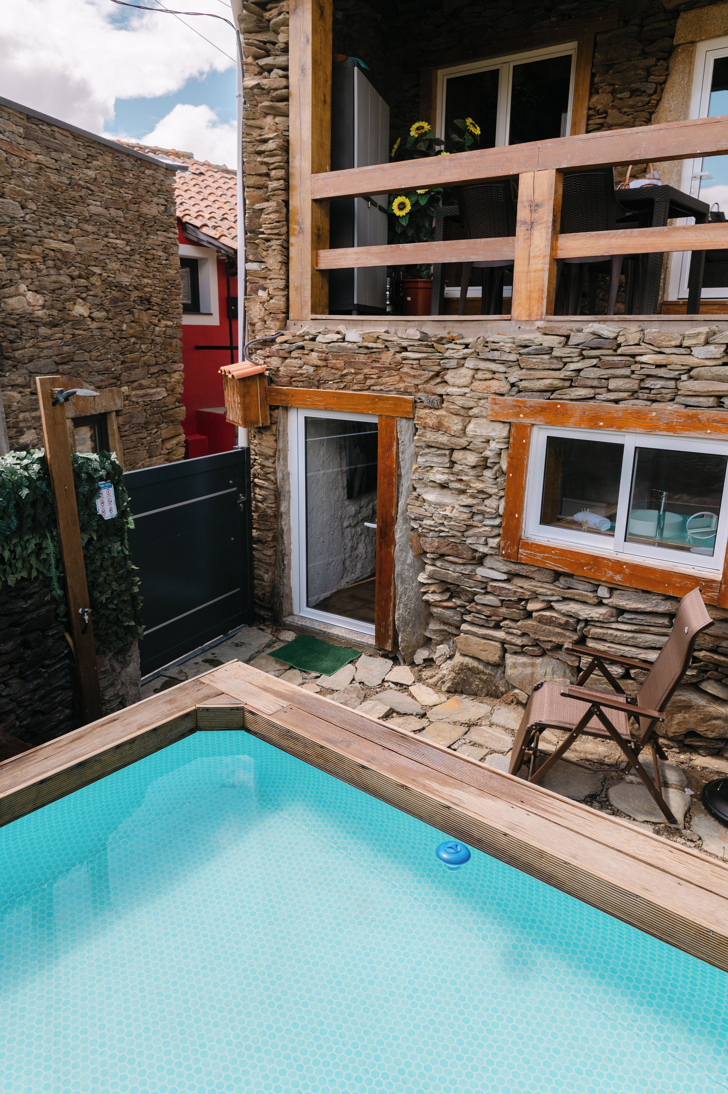 Et stenhus med swimmingpool, træterrasse og en røddoor.
