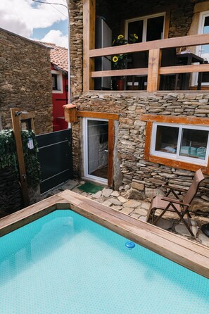 Une maison en pierre avec une piscine, une terrasse en bois et une porte rouge.