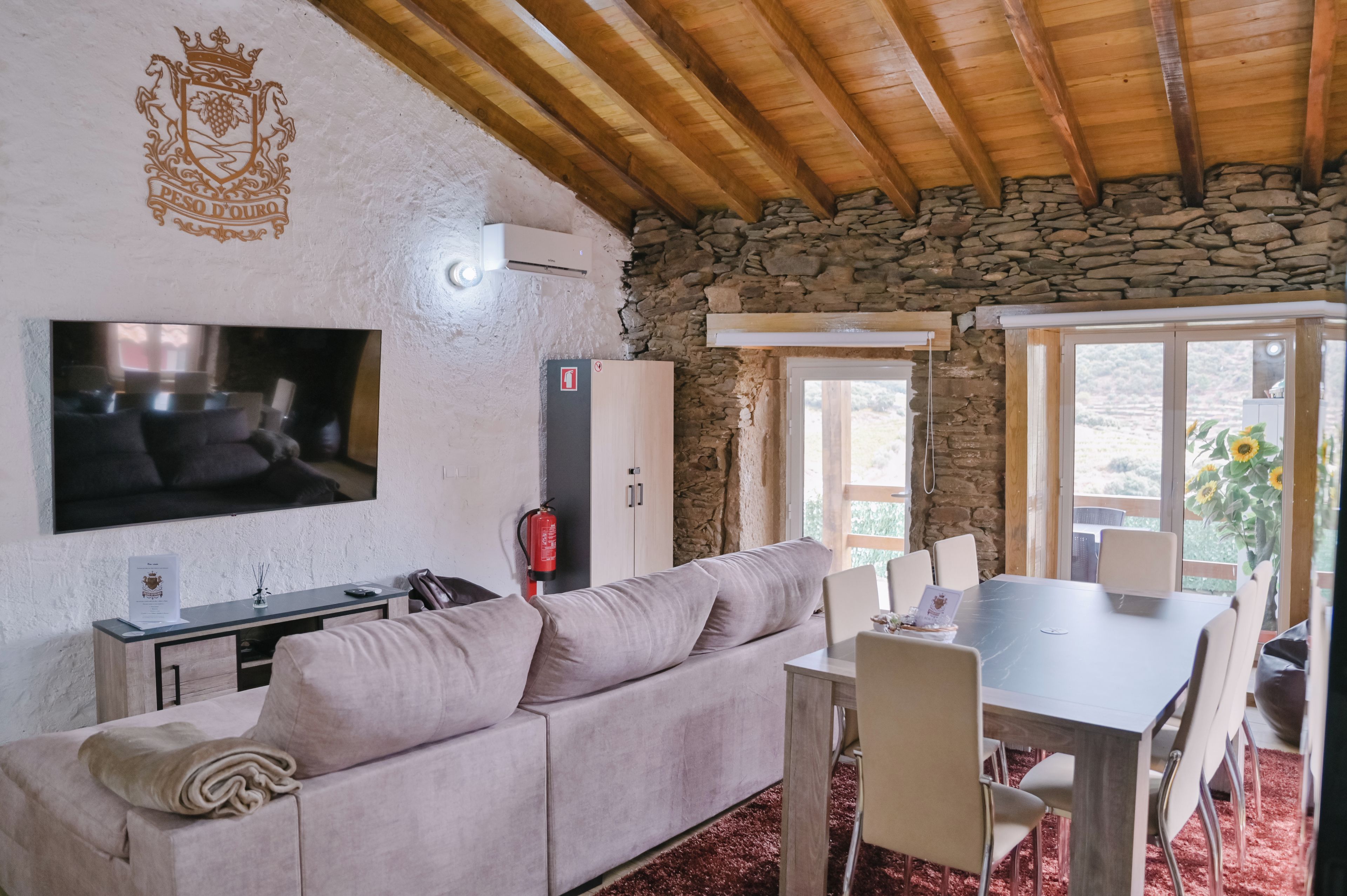 A cozy living room with a stone wall, a flat-screen TV, a sofa, a dining table with chairs, and a fire extinguisher.