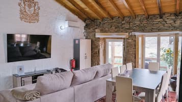 A cozy living room with a stone wall, a flat-screen TV, a sofa, a dining table with chairs, and a fire extinguisher.