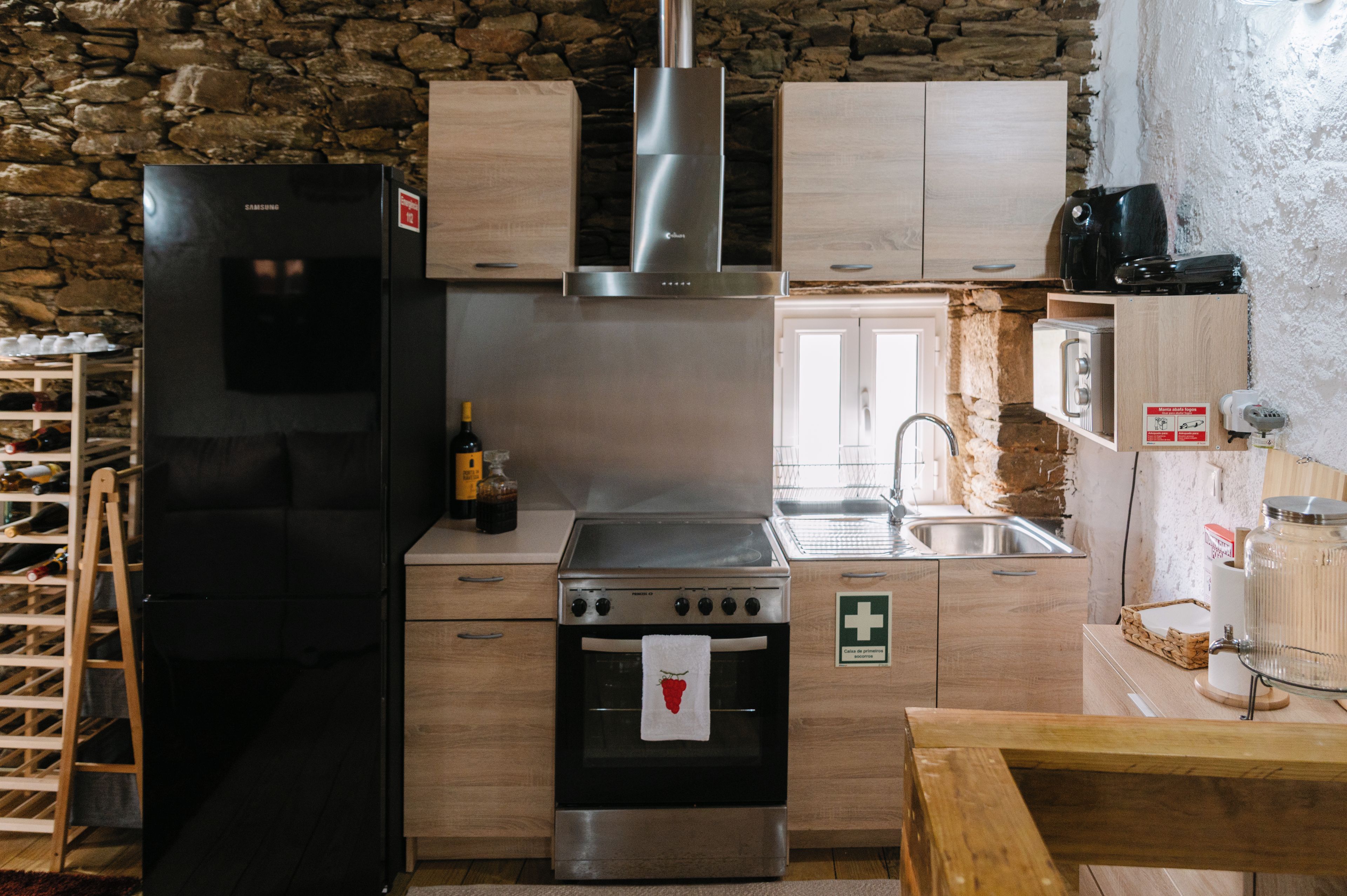 Una cocina con pared de piedra, refrigerador negro, armarios de madera, estufa de acero inoxidable y un lavaplatos.