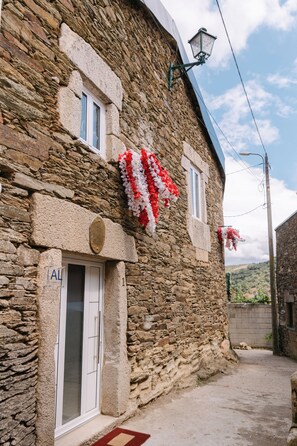 A stone building with a white door and windows, a street lamp, and a red and white floral decoration.