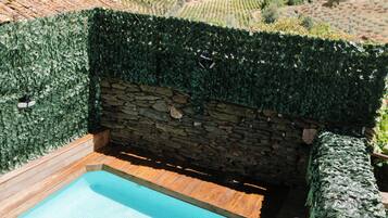 A hot tub with a stone wall and ivy-covered walls, surrounded by a wooden deck and a view of a vineyard.