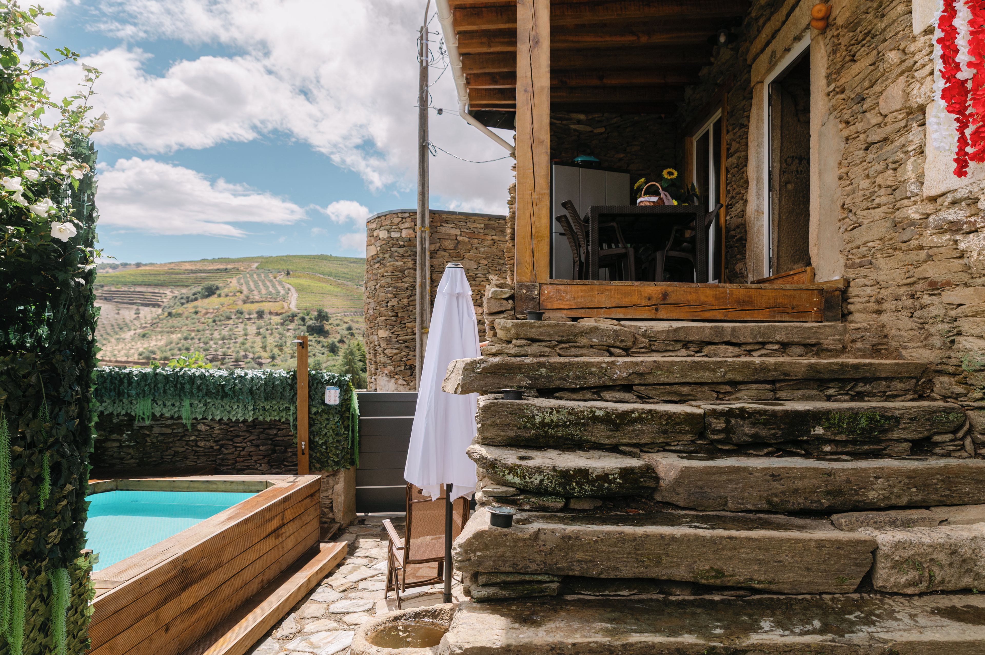 Un bâtiment en pierre avec une piscine, des marches en bois et un parasol blanc.