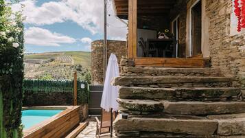 Un bâtiment en pierre avec une piscine, des marches en bois et un parasol blanc.