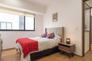 Ein Schlafzimmer mit einem Bett, einem Nachttisch, einer Lampe, einem Fenster und einem Bilderrahmen an der Wand.