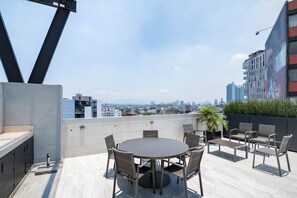Eine Dachterrasse mit rundem Tisch und Stühlen, einer kleinen Bar und Blick auf die Stadtlandschaft.