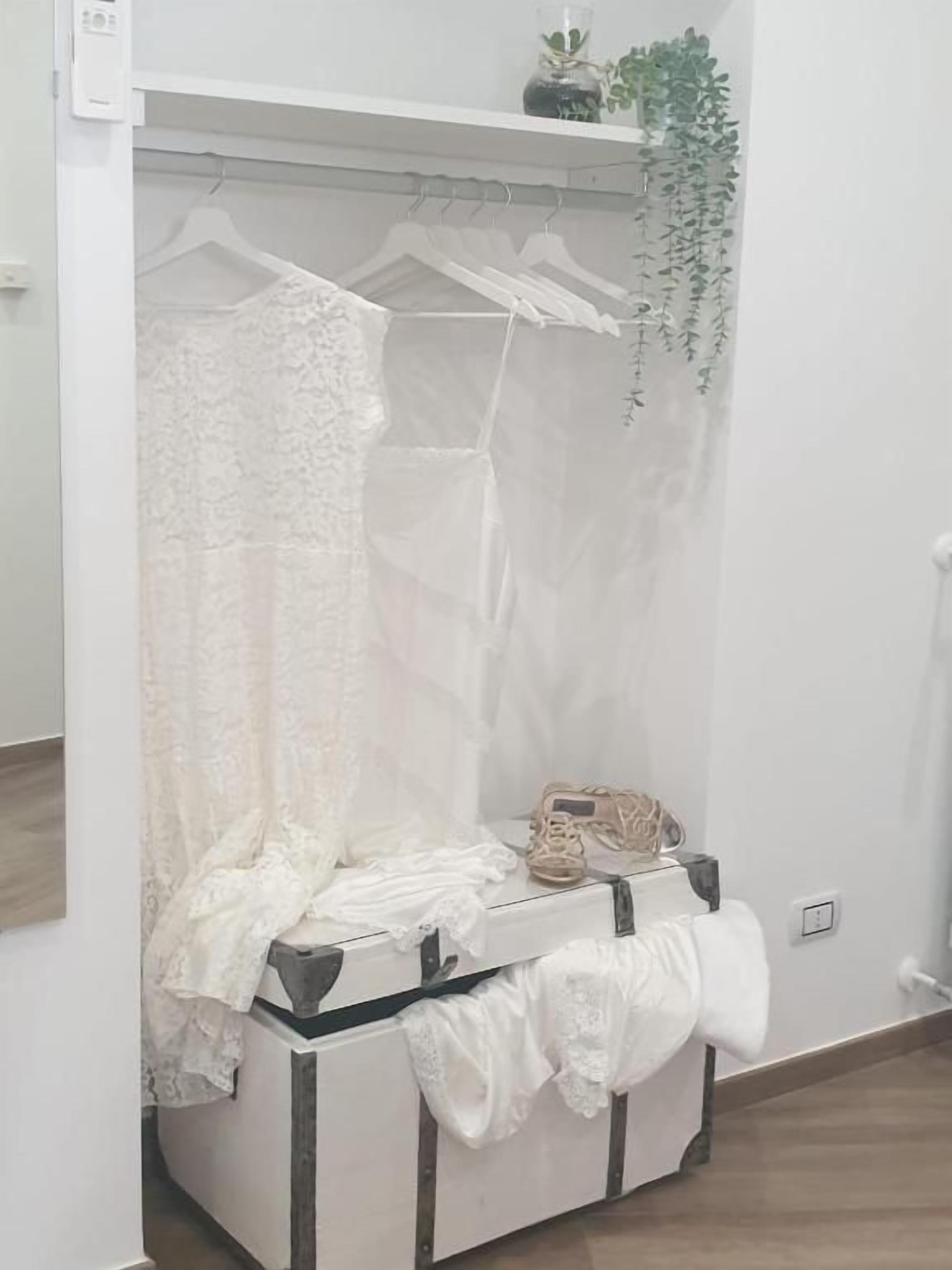 A room with a white wardrobe, a hanging plant, and a small table with a handbag and shoes.