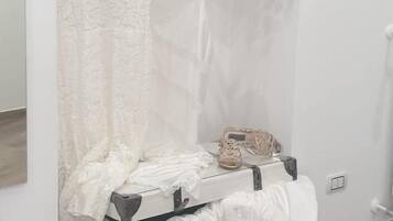 A room with a white wardrobe, a hanging plant, and a small table with a handbag and shoes.