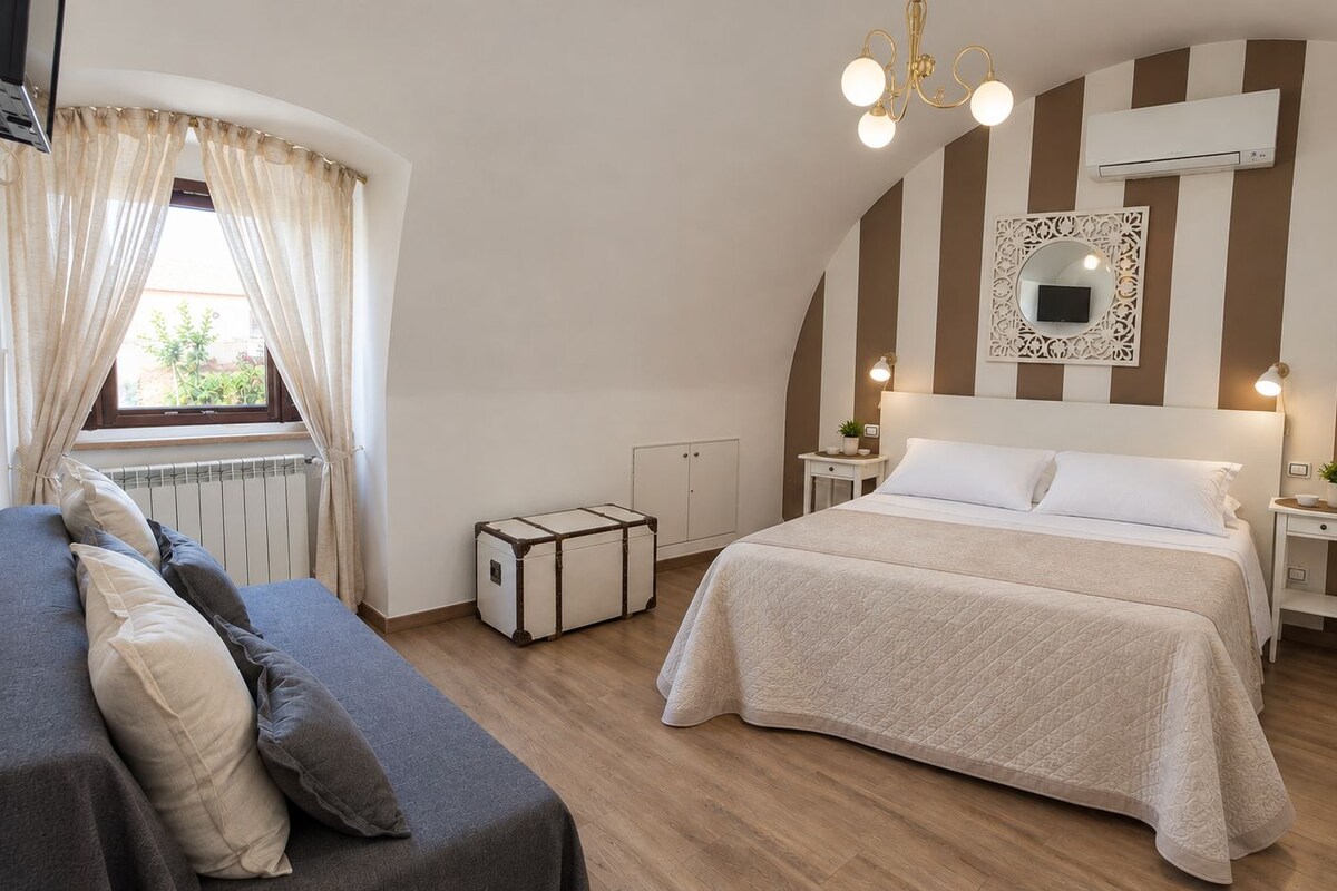 A bedroom with a bed, bedside tables, a radiator, curtains, a suitcase, and a hanging chair.