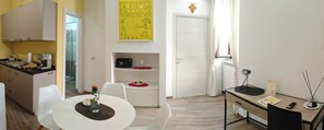 A modern kitchen with white cabinets, a dining table with chairs, a small refrigerator, and a yellow wall with a framed picture.