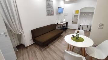 A modern living room with a brown sofa, a small white table with a green placemat, and a TV mounted on the wall.