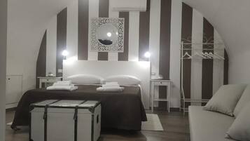 A bedroom with a bed, bedside tables, a mirror, a hanging clothes rack, and a suitcase.