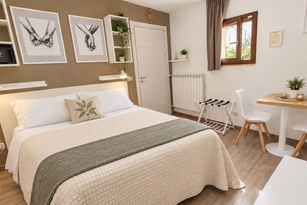 A bedroom with a bed, bedside table, and a small desk area with chairs.