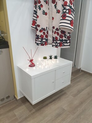 Una consola blanca con tres cajones, una pequeña planta en maceta y un difusor de cañas decorativo.