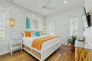 Un dormitorio con cama, mesitas de noche, ventilador de techo, una obra de arte y televisión en la pared.