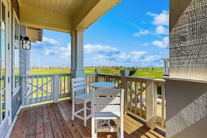 Eine Holzterrasse mit weißer Brüstung, einem Tisch und zwei Stühlen mit Blick auf einen Golfplatz.