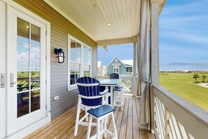 A covered porch with a table and chairs, a view of a golf course, and a house in the background. - Palmilla Beach Resort-100 Red Bay (Port Aransas)