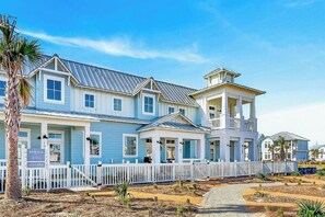 A large, two-story building with a white picket fence, a covered porch, and a small tower-like structure on the right. - Palmilla Beach Resort-102 Sea Whip Lane (Port Aransas)