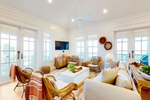 A spacious living room with a ceiling fan, large windows, and a flat-screen TV. - Palmilla Beach Resort-103 Peppervine (Port Aransas)