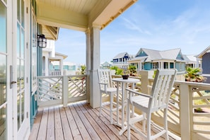 A wooden deck with white chairs and a small table, overlooking a row of beach houses. - Palmilla Beach Resort-103 Peppervine (Port Aransas)