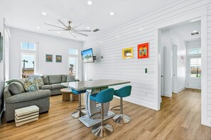 A modern kitchen with a dining area, featuring a large window, a ceiling fan, and a bar stool. - Palmilla Beach Resort-106 Sea Whip Lane (Port Aransas)