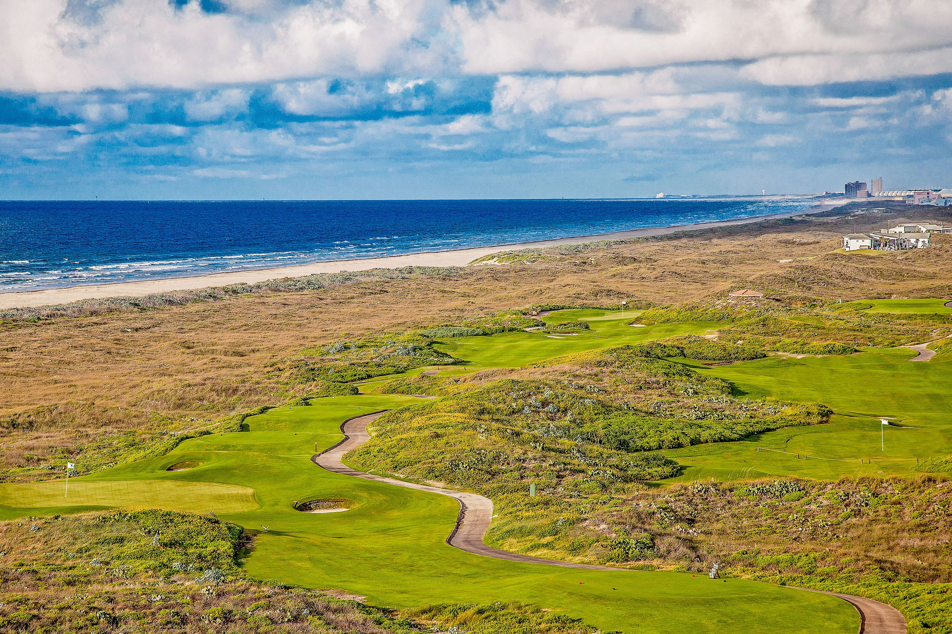 A coastal golf course with a view of the ocean and a building in the distance.