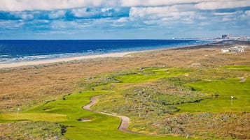 A coastal golf course with a view of the ocean and a building in the distance.
