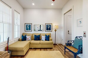 A living room with a beige sectional sofa, a blue armchair, a floor lamp, and framed artwork on the walls. - Palmilla Beach Resort-114 Cattail Street (Port Aransas)