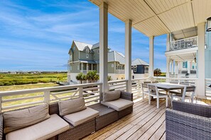 A covered outdoor deck with wicker furniture, a white railing, and a view of houses in the background. - Palmilla Beach Resort-114 Cattail Street (Port Aransas)