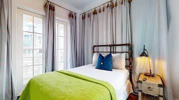 A neatly made bed with a green blanket, a wooden nightstand with a lamp, and striped curtains.