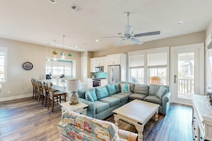 A spacious living area with a large sofa, a dining table with chairs, a kitchen area, and a ceiling fan. - Palmilla Beach Resort-114 Wild Indigo Street (Port Aransas)