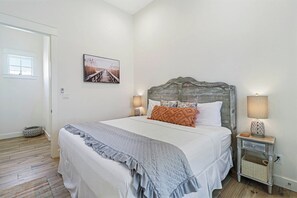 A bedroom with a large bed, a headboard, two bedside tables with lamps, a wall-mounted picture, and a door. - Palmilla Beach Resort-116 Sea Rocket Lane (Port Aransas)