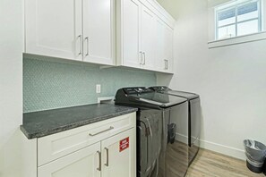 A laundry area with a washing machine, a dryer, and a fire extinguisher sign. - Palmilla Beach Resort-116 Sea Rocket Lane (Port Aransas)