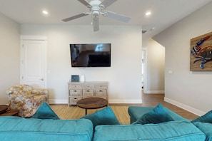 Ein Wohnzimmer mit Deckenventilator, Flachbildfernseher, Sofa, Couchtisch und einem Gemälde an der Wand.