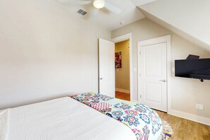 A bedroom with a bed, a ceiling fan, a TV mounted on the wall, and a door leading to another room. - Palmilla Beach Resort-118 Wild Indigo Street (Port Aransas)