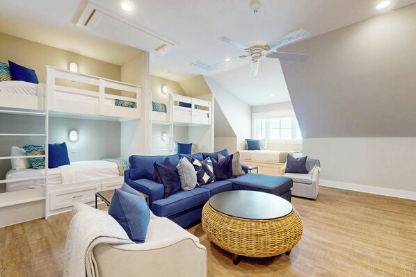 Een moderne loft slaapkamer met stapelbedden, een blauwe bank, een rond rieten bijzettafeltje en een plafondventilator.