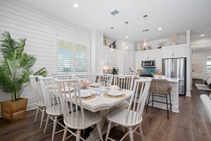 A modern kitchen with white cabinetry, a dining area with a white table and chairs, and a large potted plant. - Palmilla Beach Resort-119 Wild Indigo Street (Port Aransas)