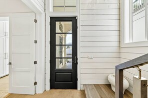 A black door with a glass panel, white walls with horizontal siding, a white bench, and a small rug. - Palmilla Beach Resort-120 Cattail Street (Port Aransas)