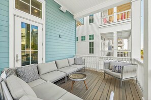 A covered porch with a grey sofa, a small round table, and a white railing. - Palmilla Beach Resort-120 Cattail Street (Port Aransas)