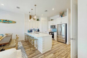 A modern kitchen with white cabinetry, stainless steel appliances, and a central island with bar stools. - Palmilla Beach Resort-121 Wild Indigo (Port Aransas)