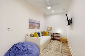 A room with a bed, a sofa, a ceiling fan, a wall-mounted TV, a painting, and a small table with a lamp. - Palmilla Beach Resort-121 Wild Indigo (Port Aransas)