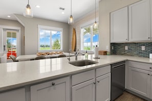 A modern kitchen with a large island, white cabinetry, and a view of the outdoors. - Palmilla Beach Resort-122 Wild Indigo Street (Port Aransas)