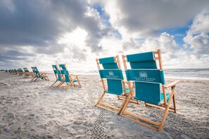 A row of beach chairs on a sandy beach with a logo on the backrest, under a partly cloudy sky. - Palmilla Beach Resort-122 Wild Indigo Street (Port Aransas)