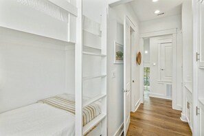 A narrow hallway with white walls, wooden flooring, and a bed with a striped bedspread. - Palmilla Beach Resort-130 Sweetbay Street (Port Aransas)