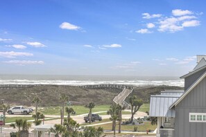 Vista costera con un paseo marítimo de madera que lleva a la playa, palmeras y un edificio con porche.